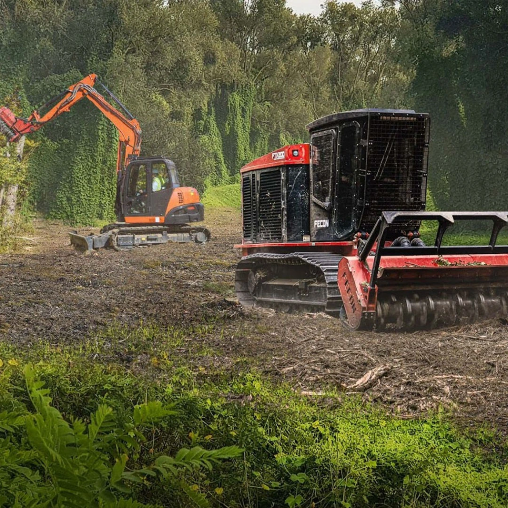 Two construction trucks clearing land in a wooded area